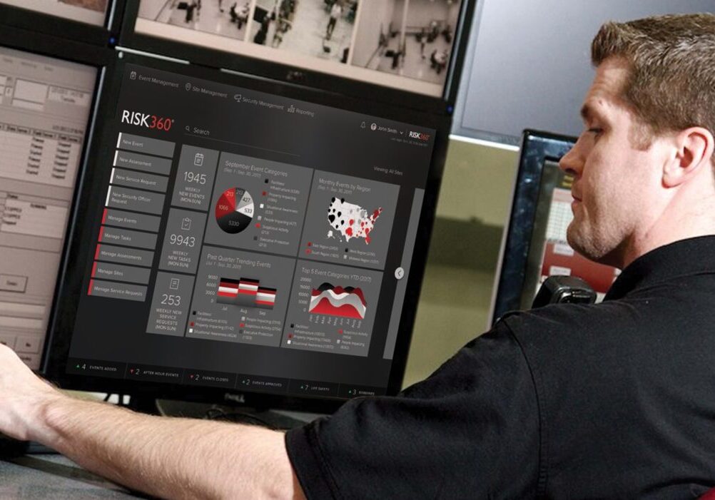 Security officer working at a desk with multiple computer screens. His back is to the camera.