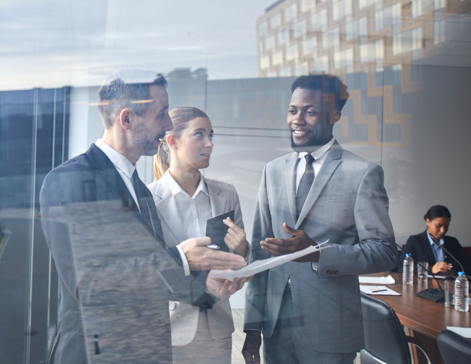 Group of two men and one woman wearing suits discussing paperwork in a conference room